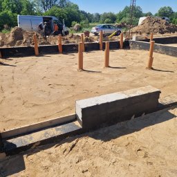 House Instal Spółka z ograniczoną odpowiedzialnością - Fundament budynku w trakcie budowy z wystającymi rurami kanalizacyjnymi, widoczny samochód dostawczy i ekipa budowlana w tle.