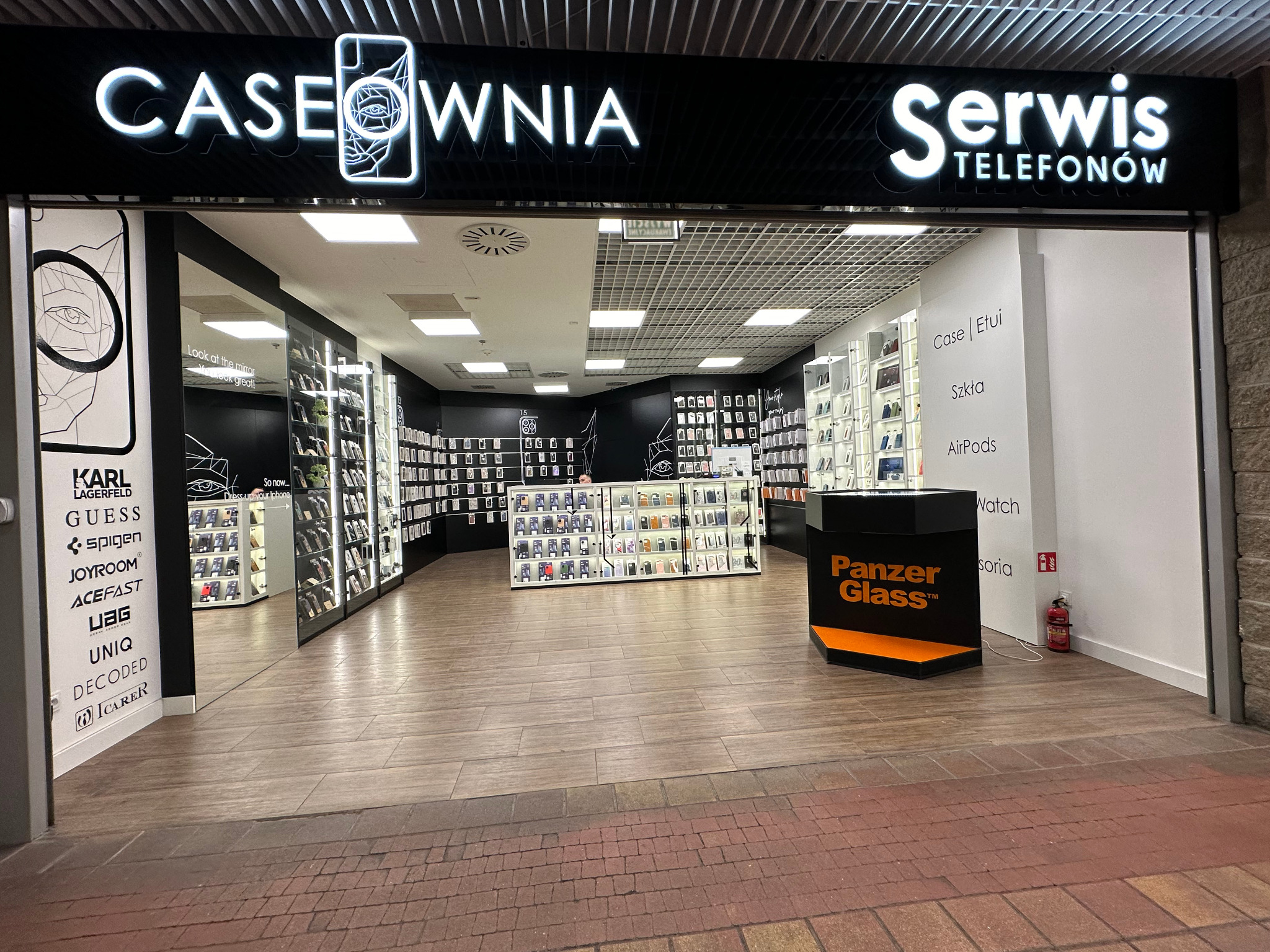 Wejście do sklepu Caseownia Serwis Telefonów z szerokim asortymentem etui i akcesoriów do telefonów, widoczne półki z produktami oraz logo Panzer Glass.