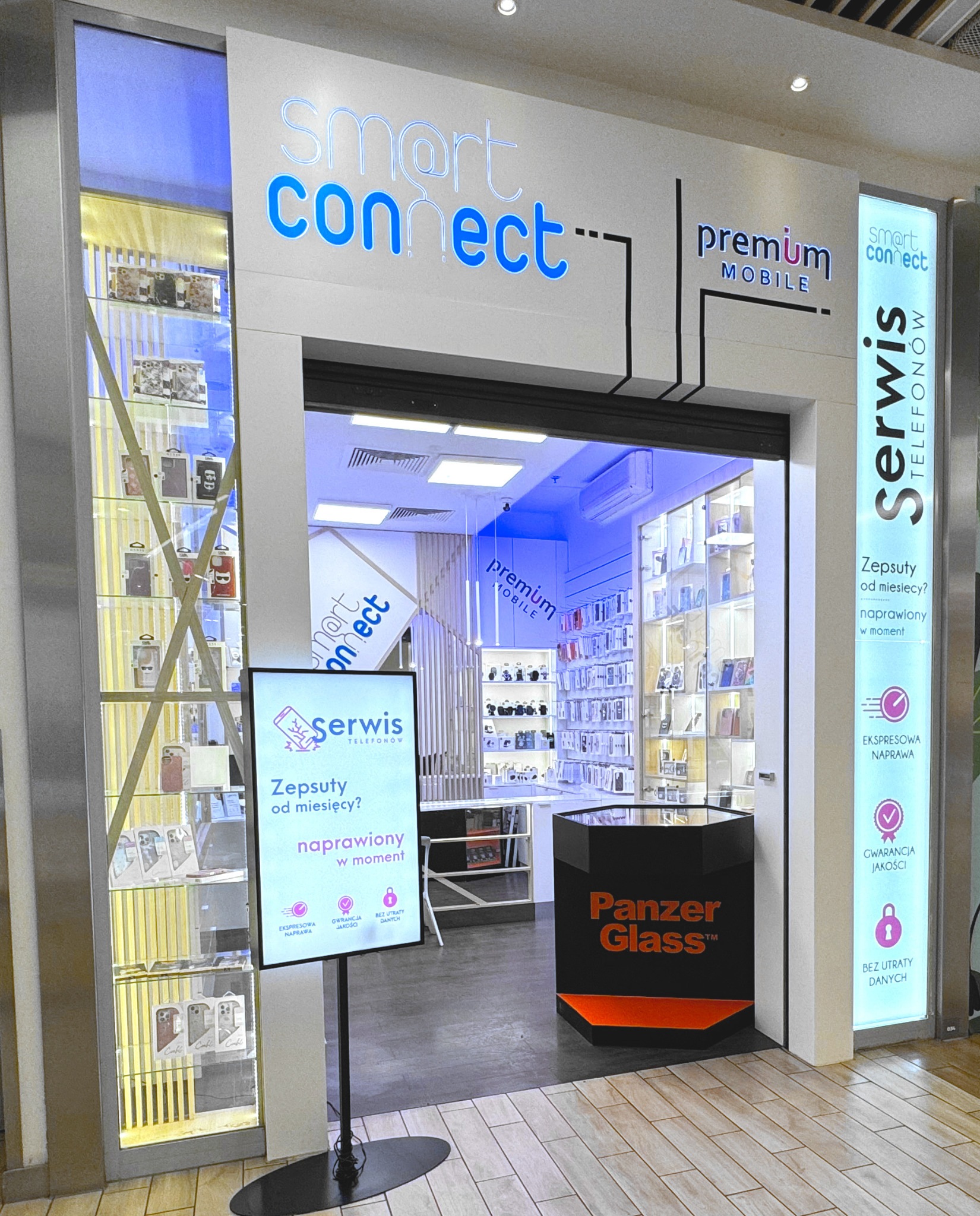 Wejście do salonu Smart Connect Premium Mobile, oferującego serwis telefonów, z ekspozycją akcesoriów w gablotach i informacją o ekspresowej naprawie oraz gwarancji jakości.