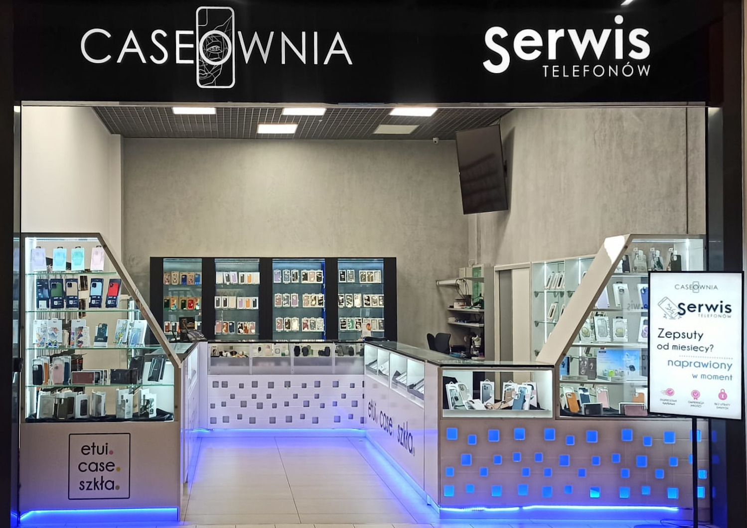 Wnętrze sklepu z akcesoriami do telefonów, prezentujące ekspozycję etui i szkieł ochronnych, oświetlone niebieskimi diodami LED, z widocznym szyldem 'CASEOWNIA Serwis TELEFONÓW'.