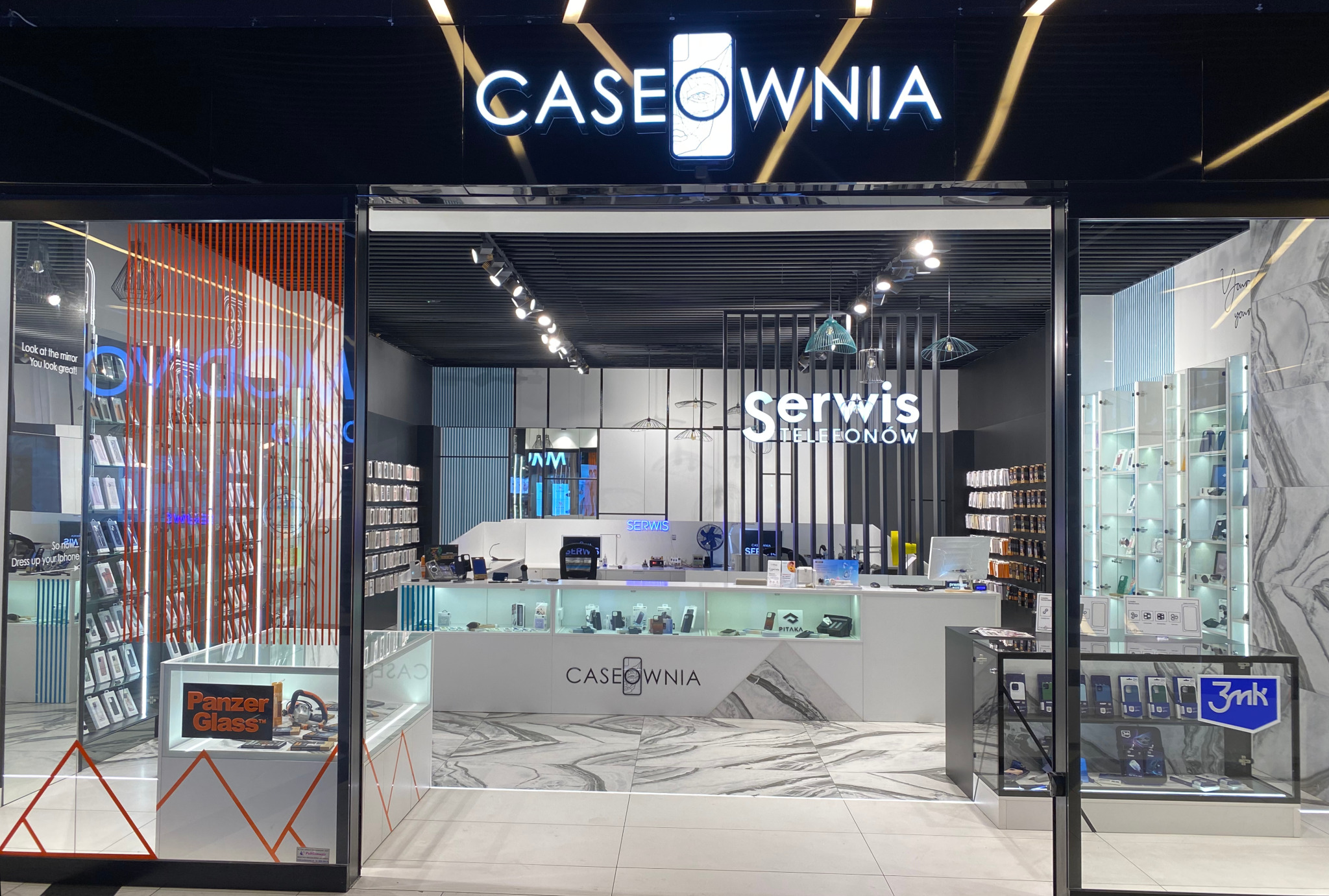 Wejście do sklepu Caseownia z neonowym szyldem i ekspozycją akcesoriów do telefonów, widoczny napis 'Serwis Telefonów' nad ladą.