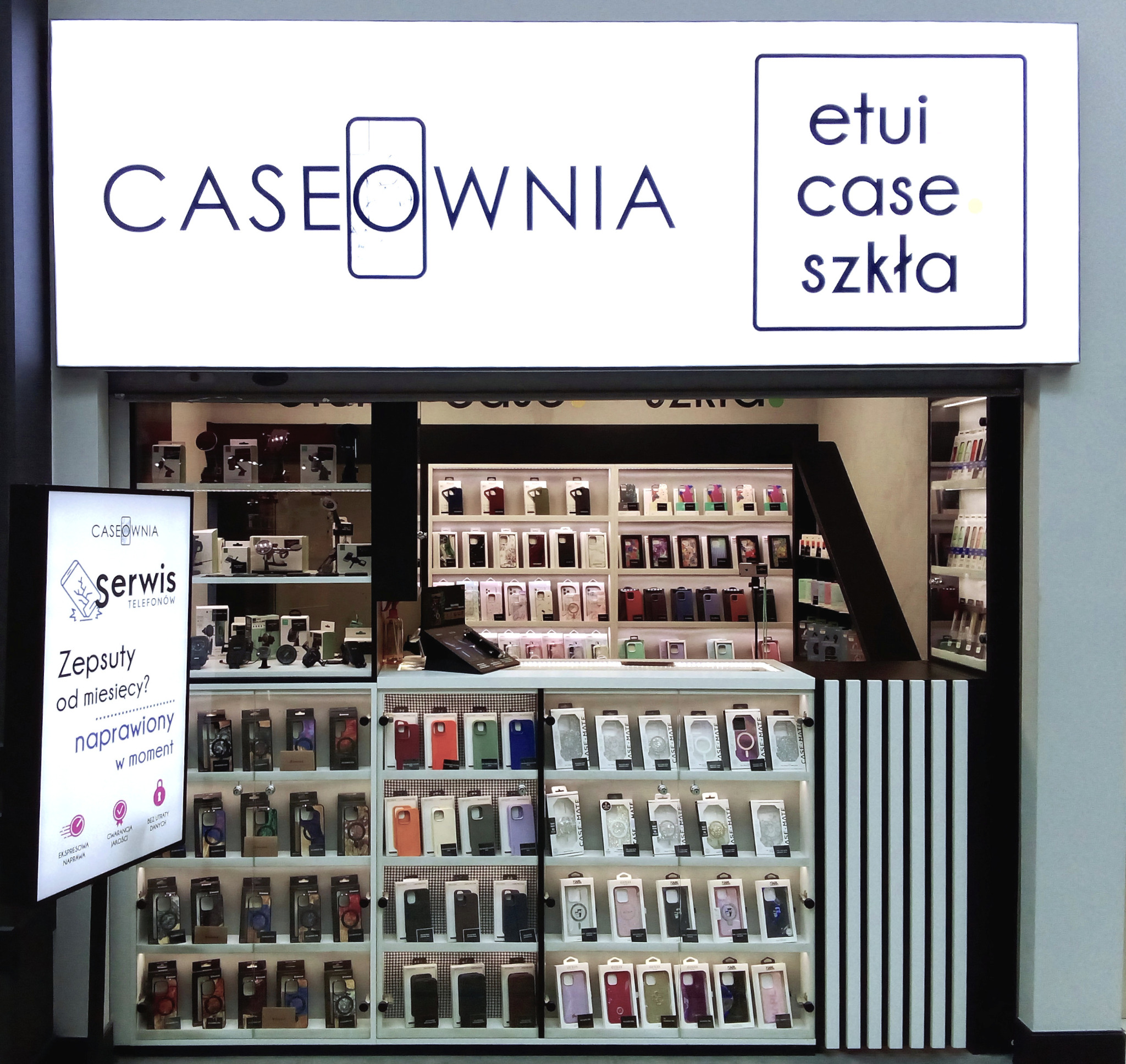 Wnętrze sklepu Caseownia z szerokim wyborem etui na telefony, akcesoriów i usług serwisowych, widoczne półki z ekspozycją produktów i tablica informacyjna o naprawie telefonów.