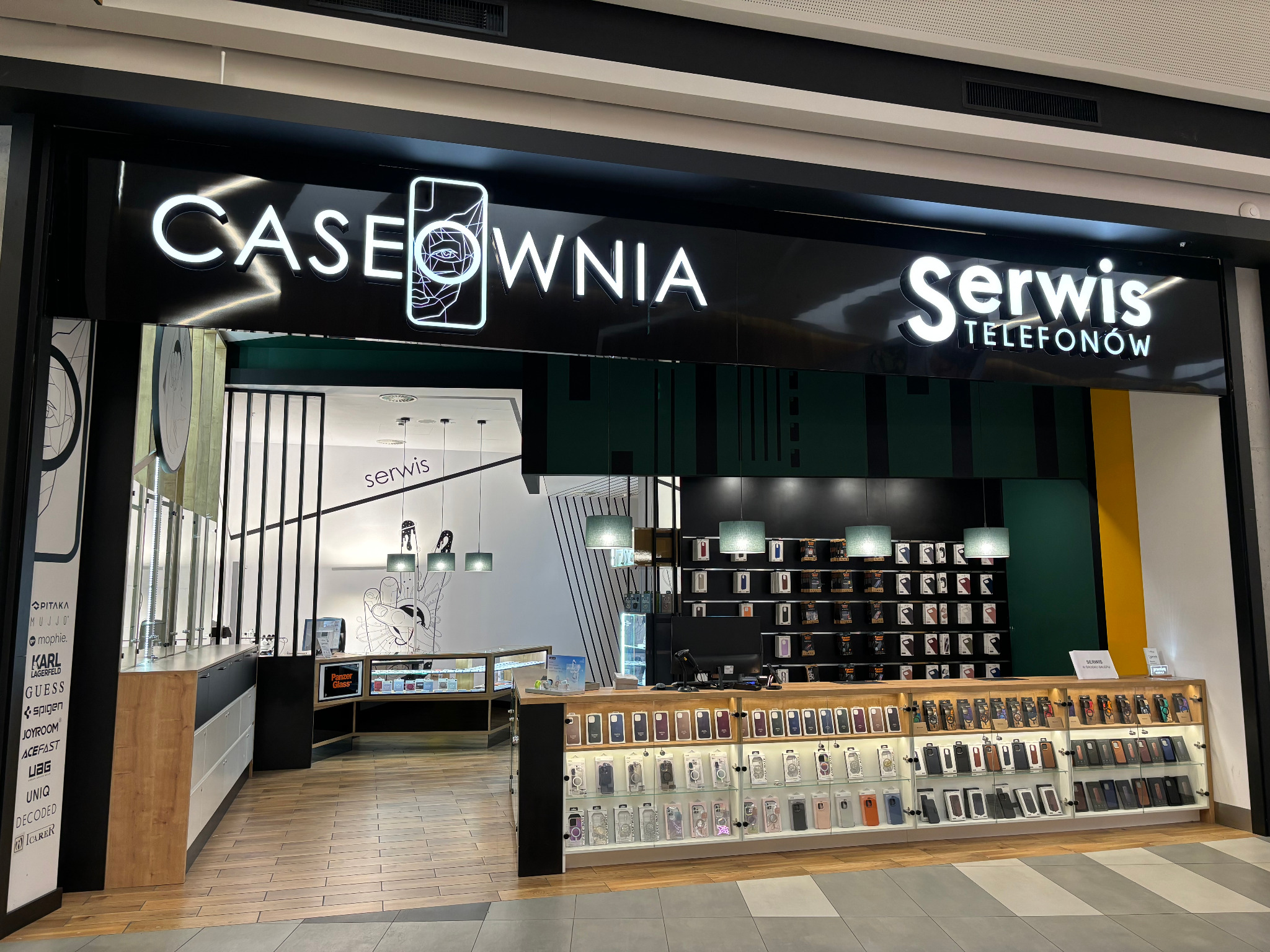 Fasada sklepu 'Caseownia Serwis Telefonów' z ekspozycją etui na telefony i akcesoriów, widoczne logo i nazwa sklepu w neonach.