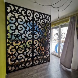Firma Remontowo-Usługowa Bartłomiej Morawiec - Balustrady ażurowe - Dekoracyjna, ażurowa ścianka działowa z czarnego metalu z motywem roślinnym, oddzielająca przestrzeń w nowoczesnym wnętrzu z widokiem na balkon.