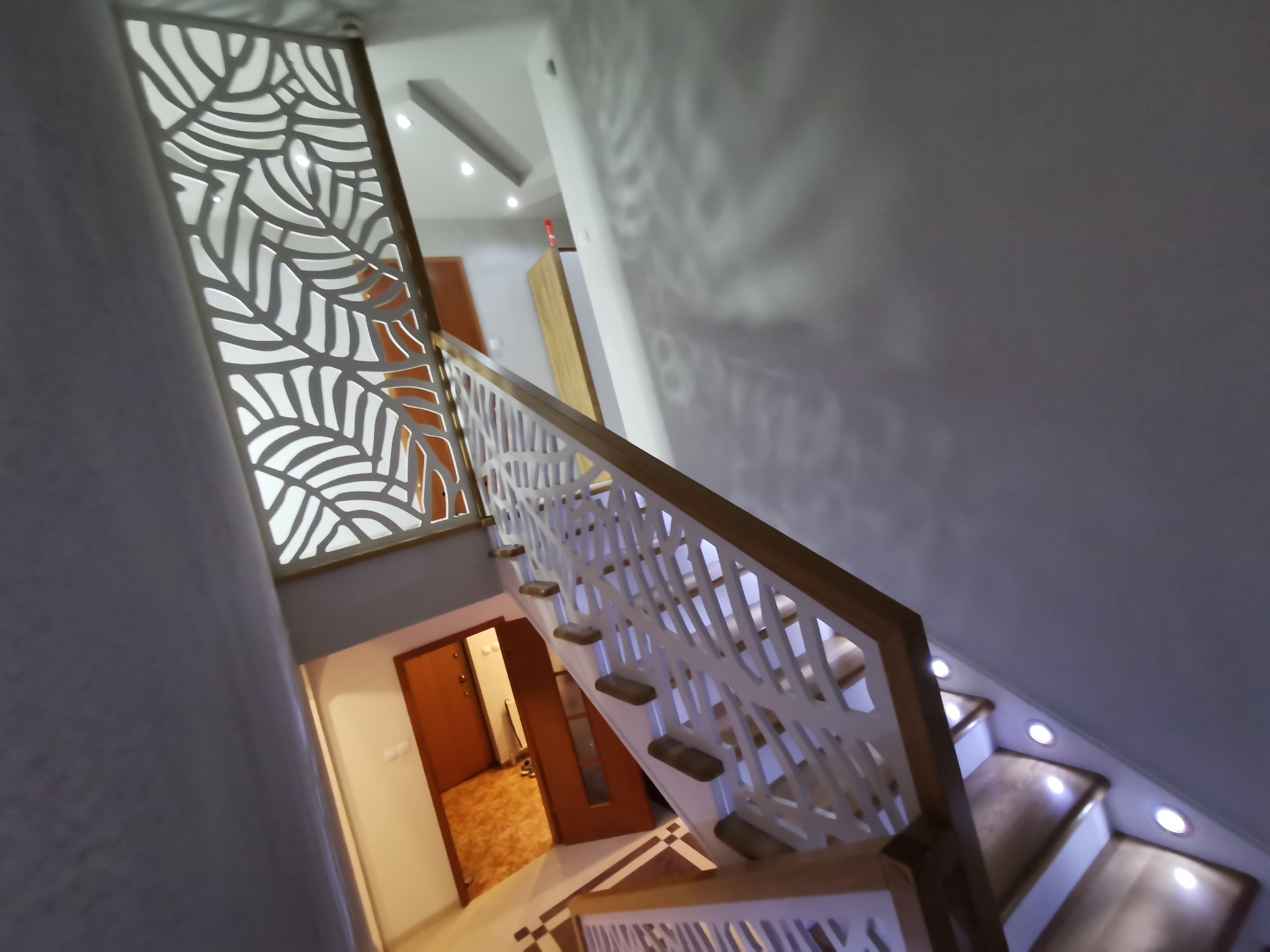 Nowoczesne schody z ażurową balustradą o wzorze liści, podświetlane stopnie, widok z góry.