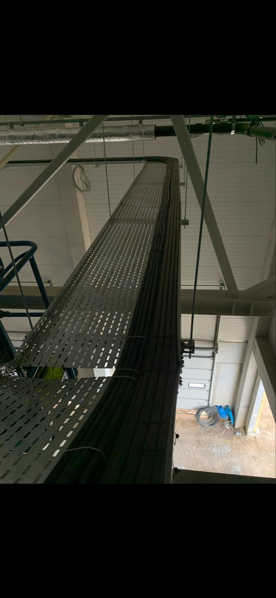 Metalowa korytka kablowa z ułożonymi kablami elektrycznymi, widok od dołu, surowy stan wykończenia wnętrza, brama garażowa w tle.