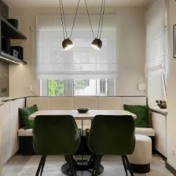 Jasna jadalnia z kremową zabudową, zielonymi poduszkami i krzesłami, oświetlona wiszącymi lampami nad stołem, z oknem przesłoniętym delikatną, białą tkaniną w stylu rolety rzymskiej.