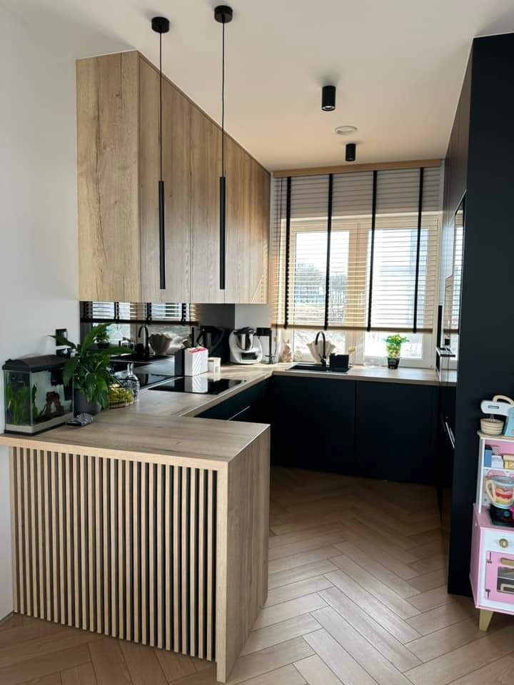 Nowoczesna kuchnia w odcieniach drewna i granatu z drewnianymi żaluzjami poziomymi z czarnymi taśmami, akwarium na blacie i podłogą w jodełkę.