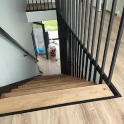 Nowoczesne schody drewniane z czarną balustradą w Bystrzycy Kłodzkiej. Widok z góry, ukazujący jasne stopnie i minimalistyczny design.