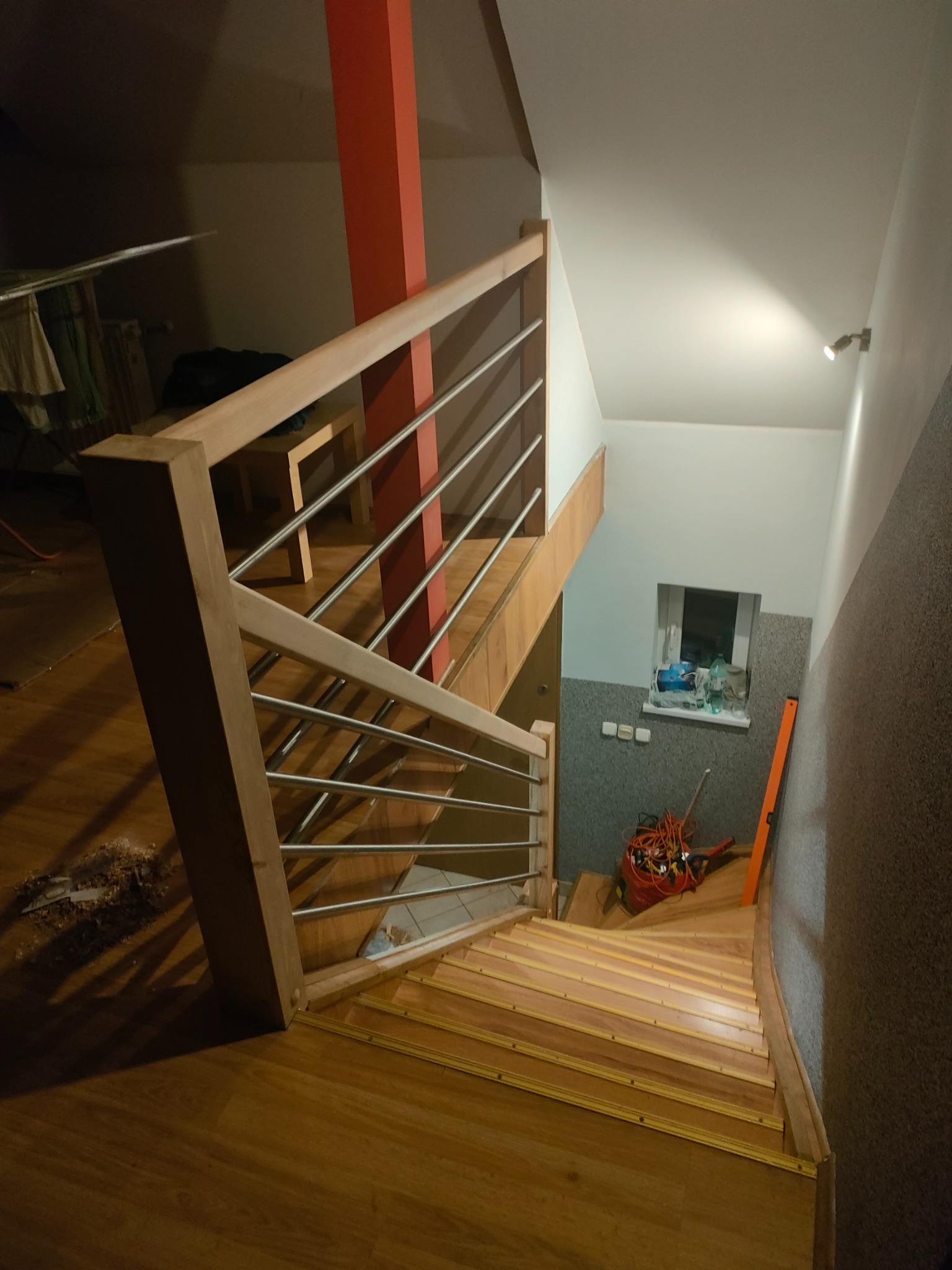 Klatka schodowa z drewnianymi stopniami i metalową balustradą, widok z góry. Na dole schodów widoczne narzędzia i poziomica.