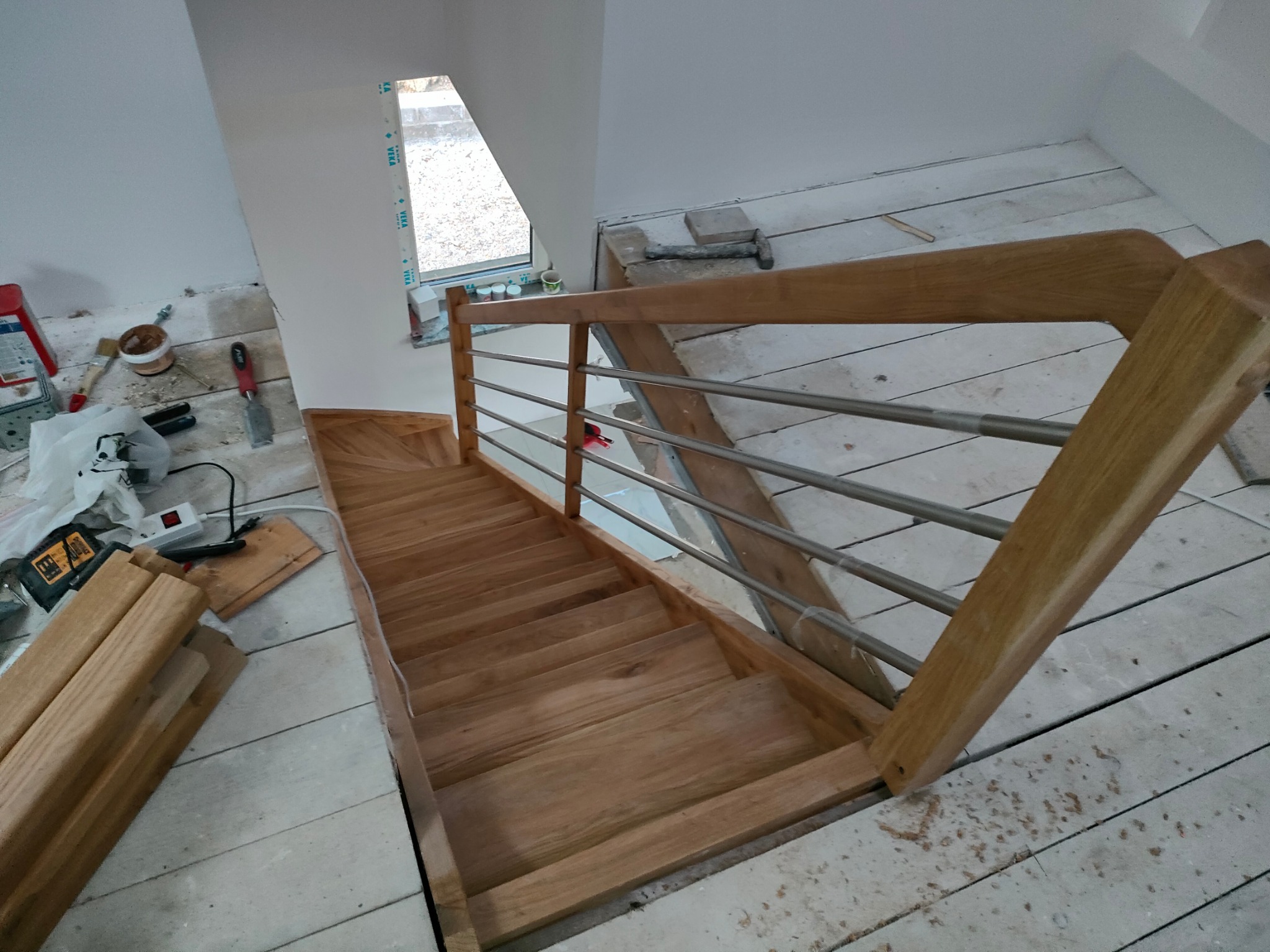 Jasne schody z drewna i metalu w trakcie montażu, widoczne narzędzia i materiały budowlane. Ujęcie z góry, ukazujące detale konstrukcji i etap prac wykończeniowych.