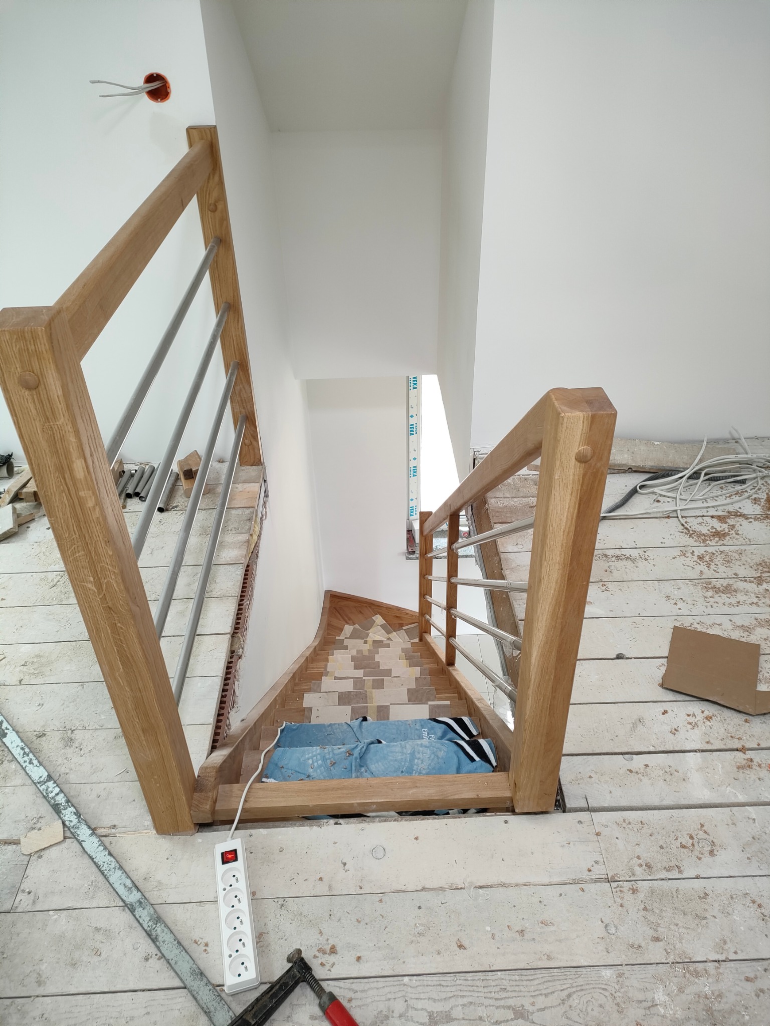 Montaż drewnianych schodów z metalowymi barierkami w surowym wnętrzu. Widoczne narzędzia i materiały budowlane. Etap wykończeniowy, widok z góry.