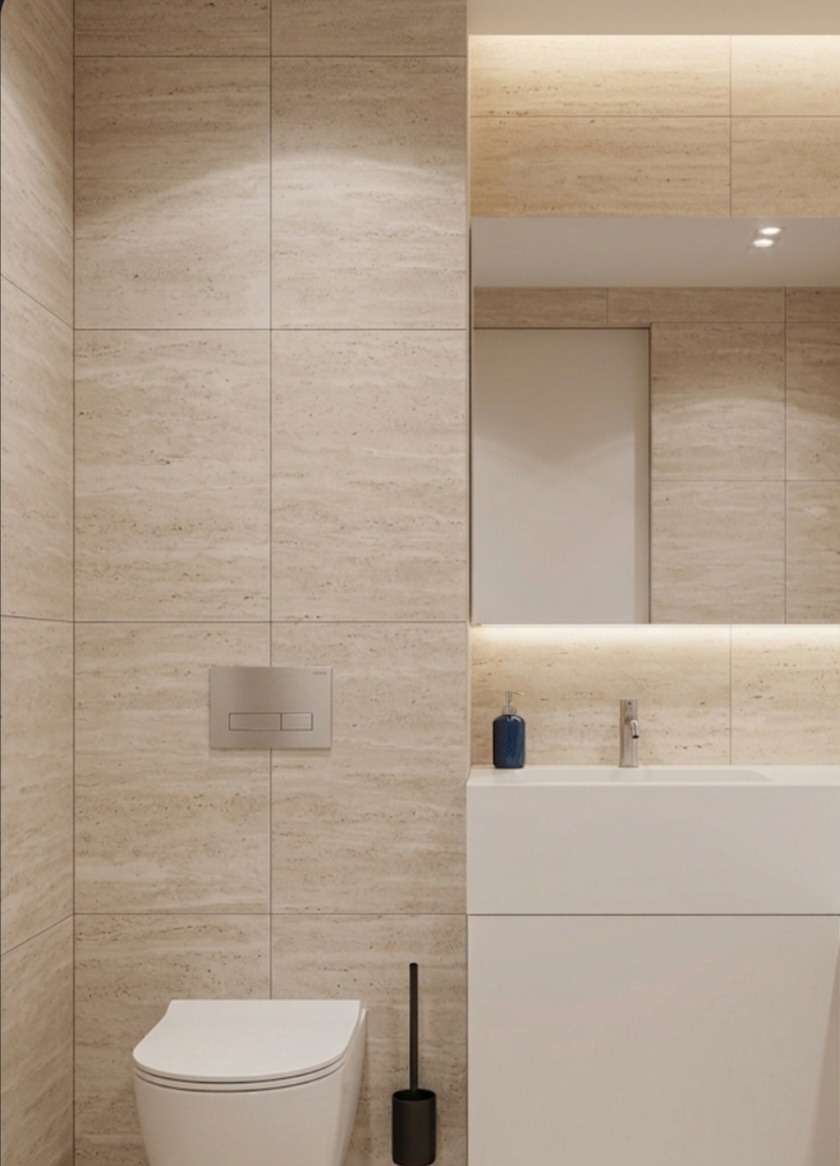 Nowoczesna łazienka z beżowymi płytkami imitującymi trawertyn, podświetlane lustro, biała umywalka i toaleta. Minimalistyczny design, ciepłe oświetlenie.