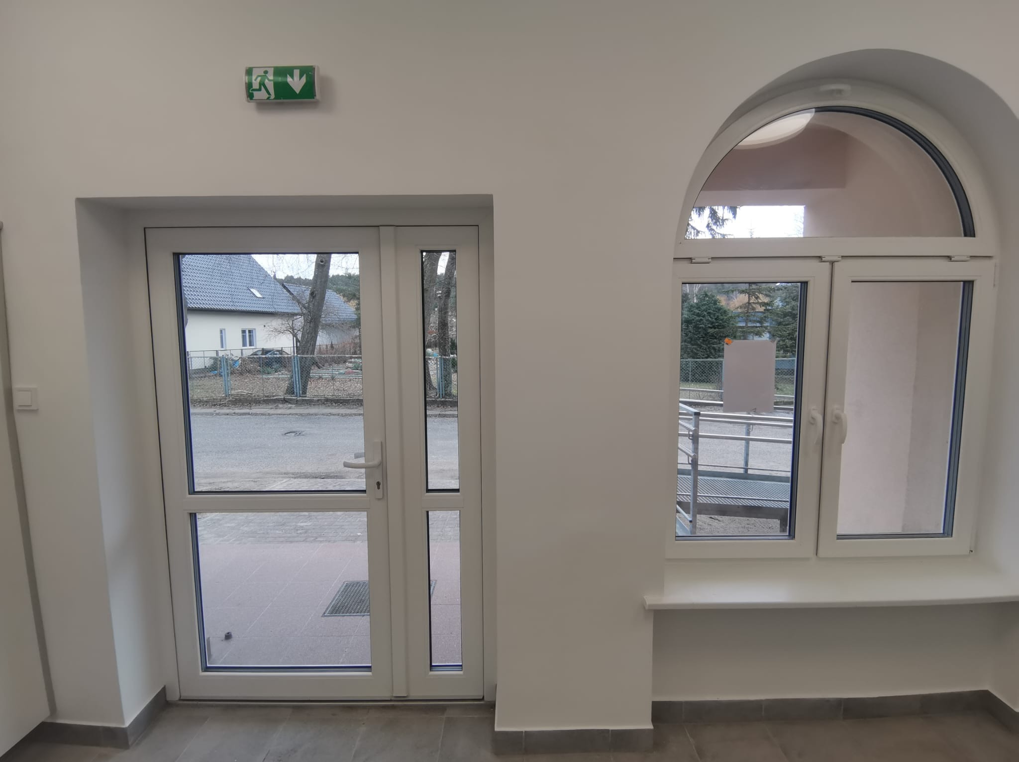 Białe drzwi wejściowe z przeszkleniami i okno łukowe w nowo wykończonym, jasnym pomieszczeniu, widok na zewnątrz