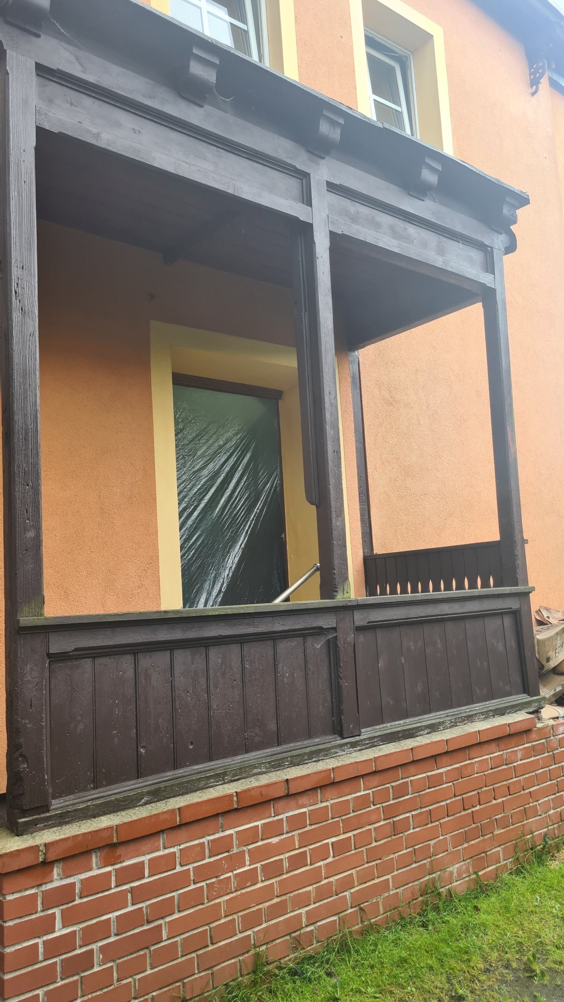 Przygotowanie drewnianej werandy do renowacji; okno zabezpieczone folią, widoczne ślady użytkowania na konstrukcji.