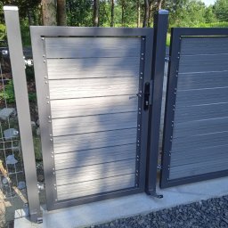 ADM Usługi Spawalnicze - Nowoczesna brama wjazdowa z szarego metalu i paneli imitujących drewno, widoczna z bliska, z fragmentem ogrodzenia siatkowego w tle.