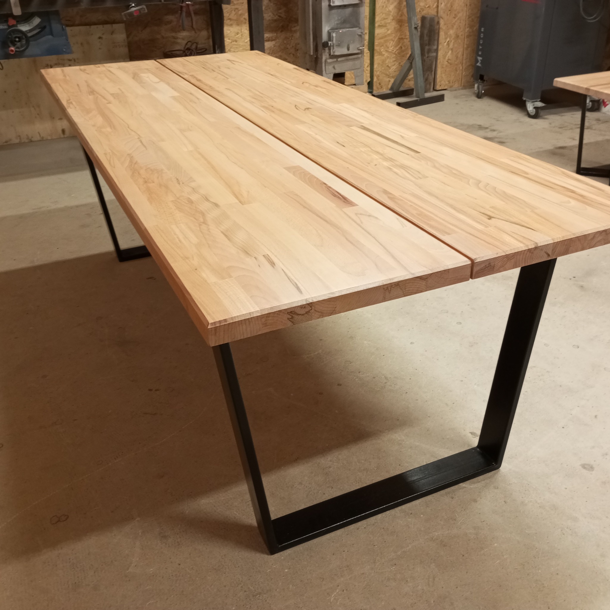 Stół z jasnego drewna z czarnymi, metalowymi nogami w warsztacie w Bolesławcu, widoczne łączenie dwóch desek blatu.
