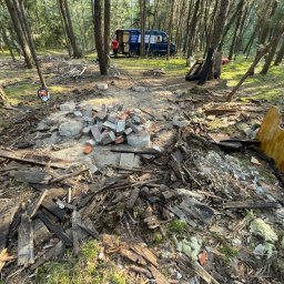 W001 SPÓŁKA Z OGRANICZONĄ ODPOWIEDZIALNOŚCIĄ - Teren po usunięciu konstrukcji w lesie, widoczne resztki drewna, cegieł, izolacji, piła łańcuchowa i samochód dostawczy w tle.