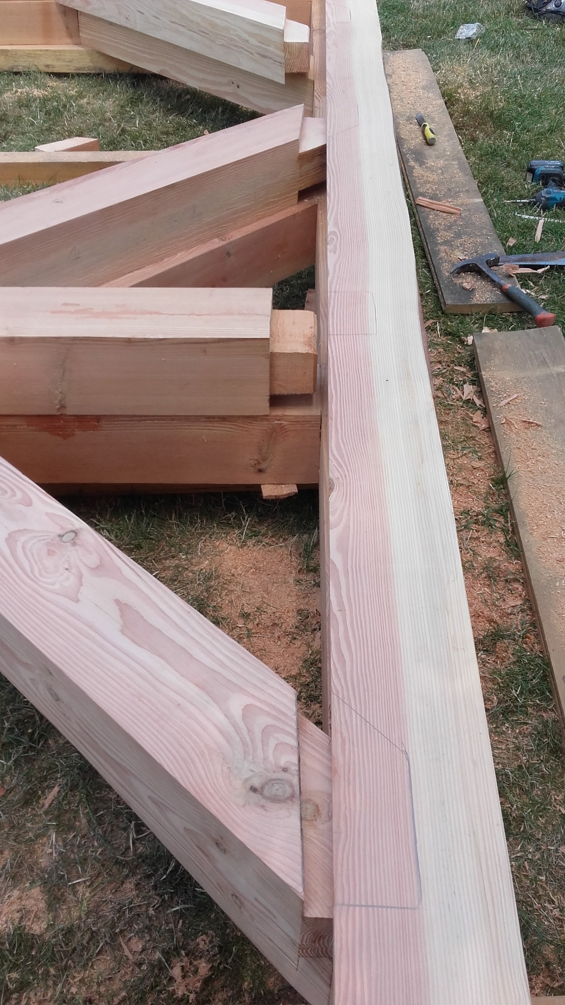 Elementy drewnianej konstrukcji w trakcie montażu, widoczne narzędzia i zarys cięcia na jednym z belek