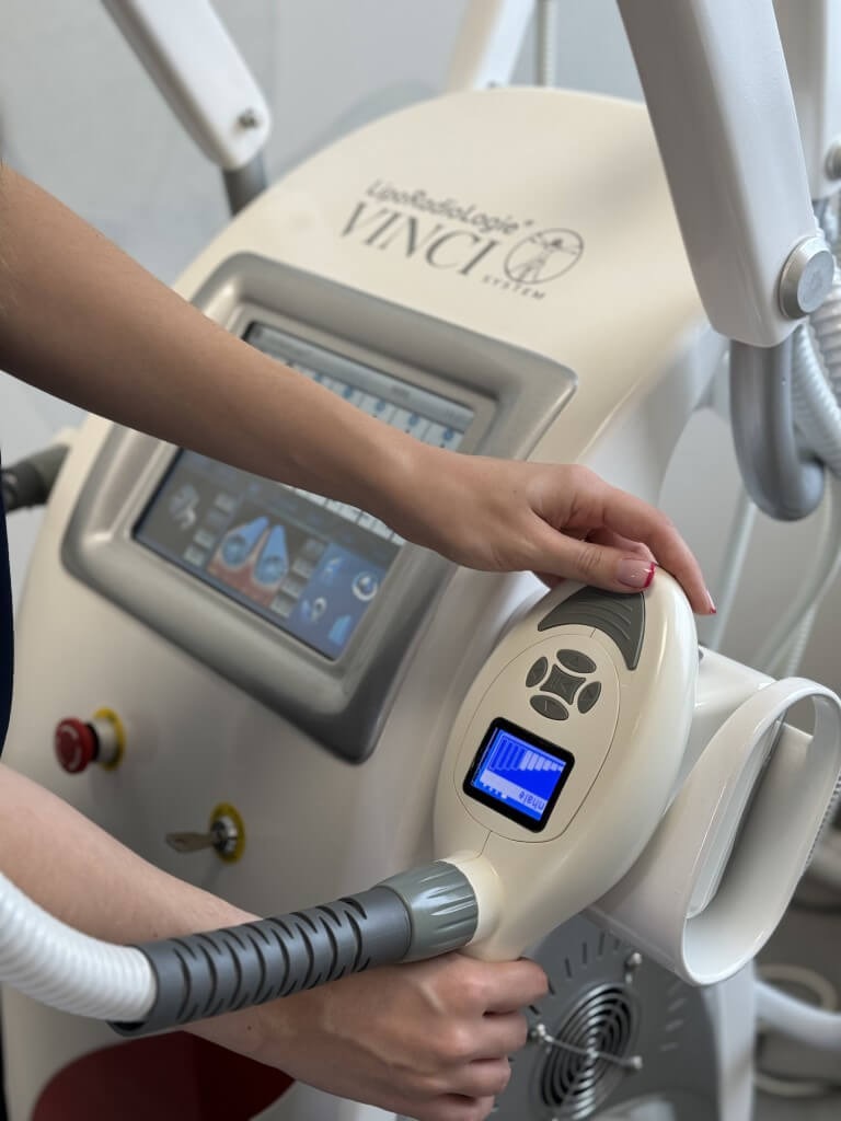 Obsługa panelu sterowania urządzenia LipoRadiologie Vinci System z ekranem dotykowym i głowicą zabiegową, widoczne dłonie operatora i fragment obudowy maszyny.