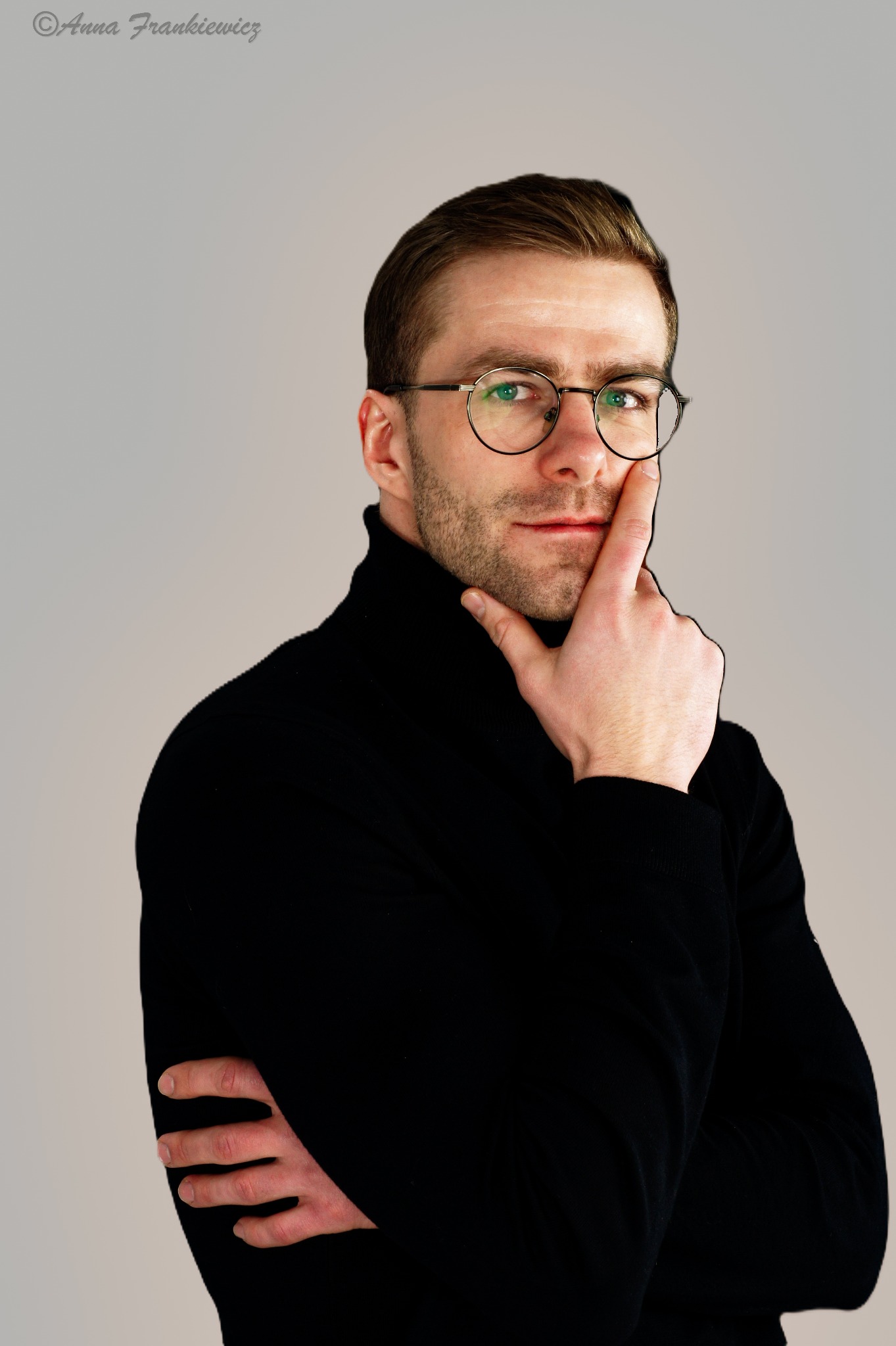 Portret mężczyzny w czarnym golfie i okularach, zamyślony wyraz twarzy, na neutralnym tle w Krakowie.