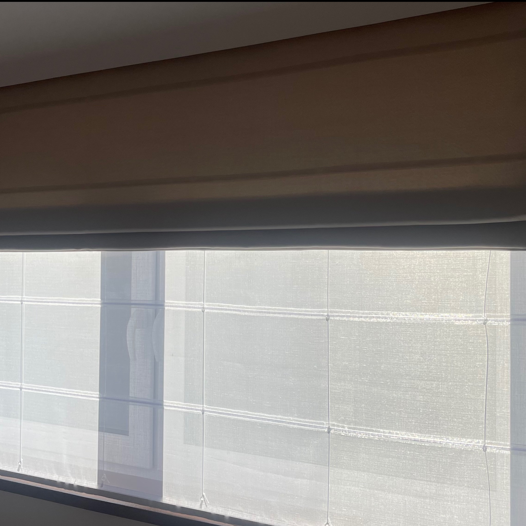 Jasna, teksturowana osłona okienna w stylu rzymskim, częściowo opuszczona, z widocznymi sznurkami i delikatnym światłem słonecznym padającym na powierzchnię.