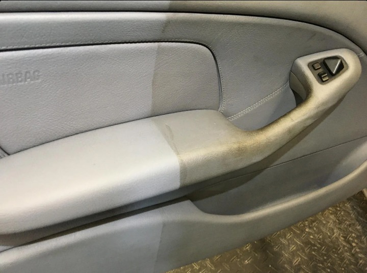 Wnętrze samochodu z szarą tapicerką drzwi w trakcie czyszczenia, widoczna wyraźna różnica między wyczyszczoną a brudną częścią, zwłaszcza na uchwycie i panelu sterowania szybami.