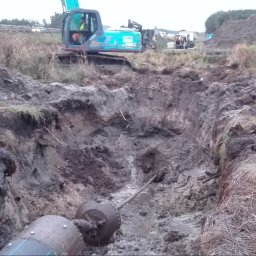COBER s.c. - Wykonany wykop pod rurę z widocznym przewiertem, w tle maszyna budowlana i usypana ziemia.