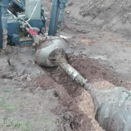 Przewiert sterowany w trakcie pracy: głowica wiertnicza zagłębiona w ziemi, widoczne błoto i wykop, maszyna wiertnicza w tle.