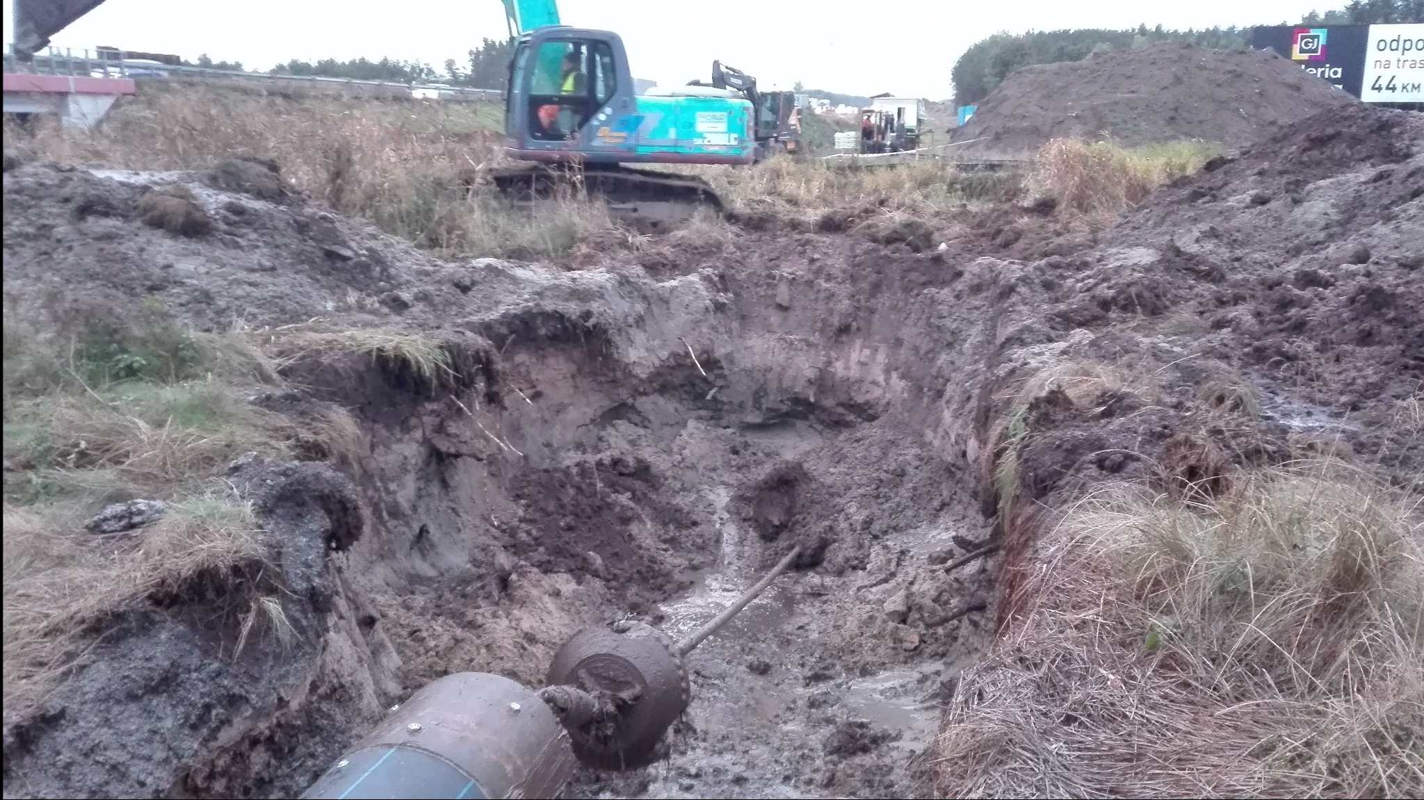 Wykonany wykop pod rurę z widocznym przewiertem, w tle maszyna budowlana i usypana ziemia.