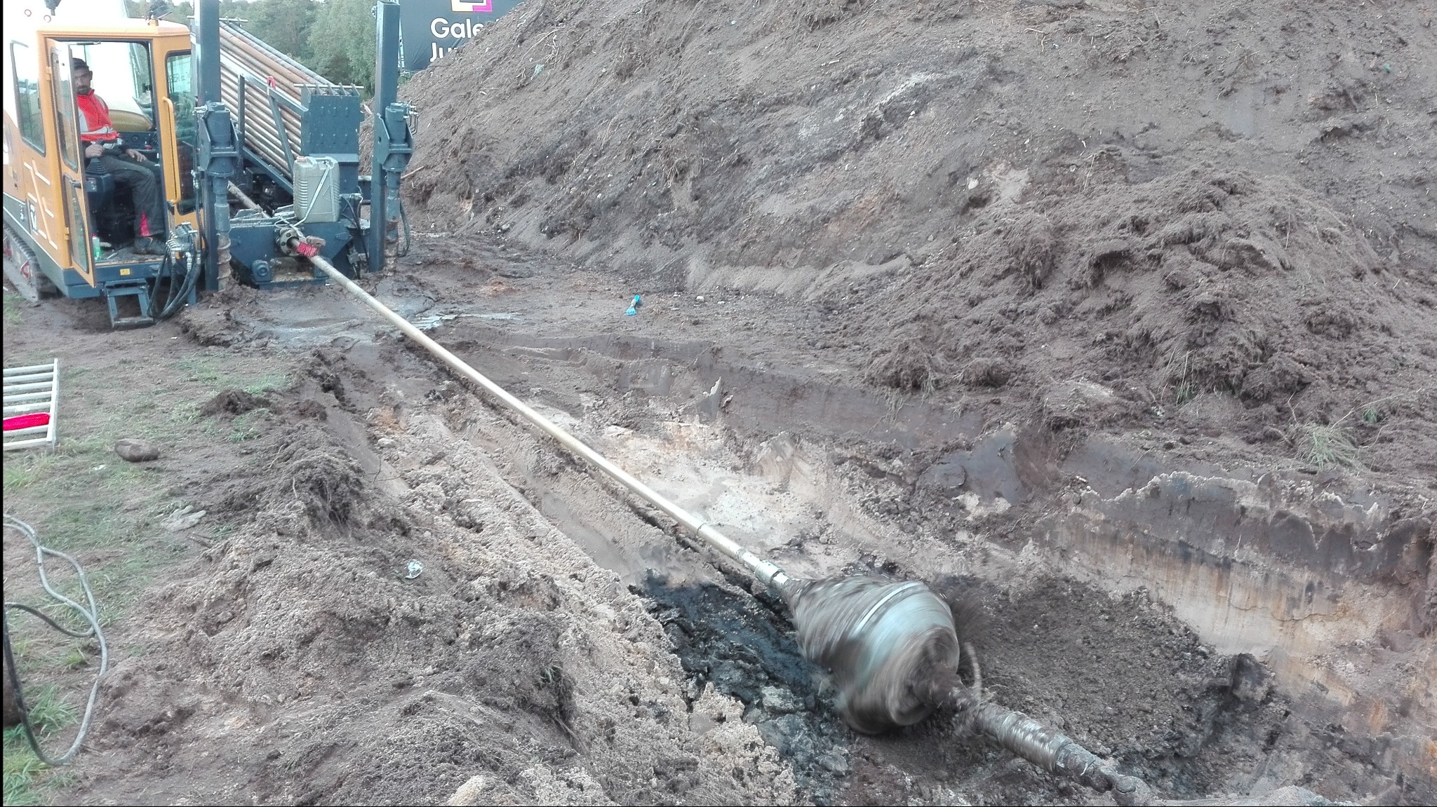 Praca w ziemi: wiertnica kierunkowa w trakcie wiercenia pod ziemią, widoczny obrotowy świder i operator w kabinie maszyny.