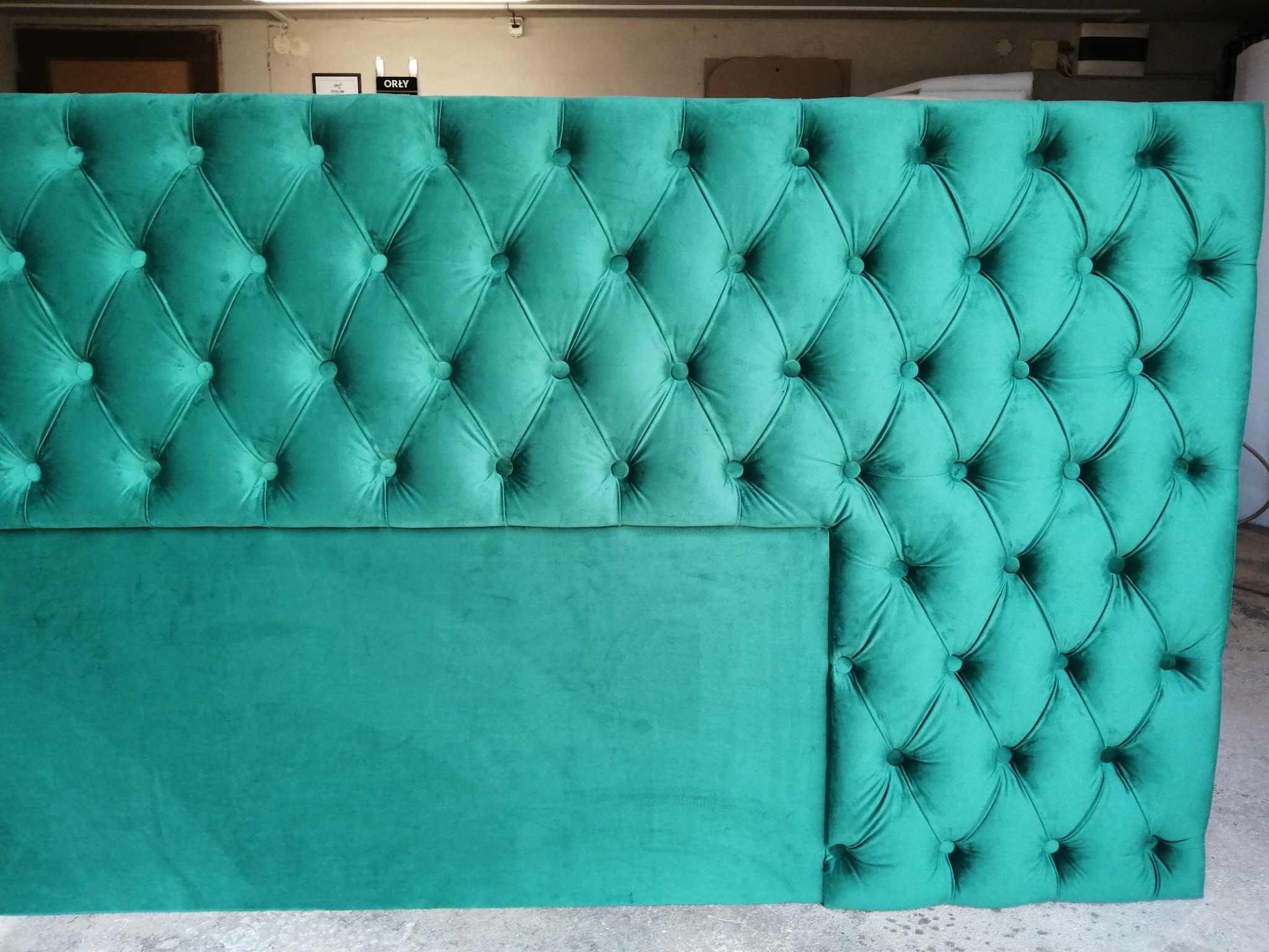 Szmaragdowy zagłówek tapicerowany z pikowaniem w romby i guzikami, częściowo bez pikowania, prezentowany w warsztacie.