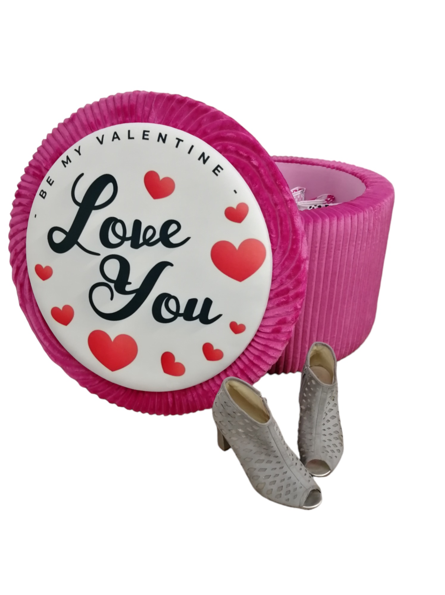 Otwierany, okrągły, różowy puf tapicerowany z napisem 'Be my Valentine Love You' i czerwonymi sercami, obok para szarych botków na obcasie z ażurowym wzorem.