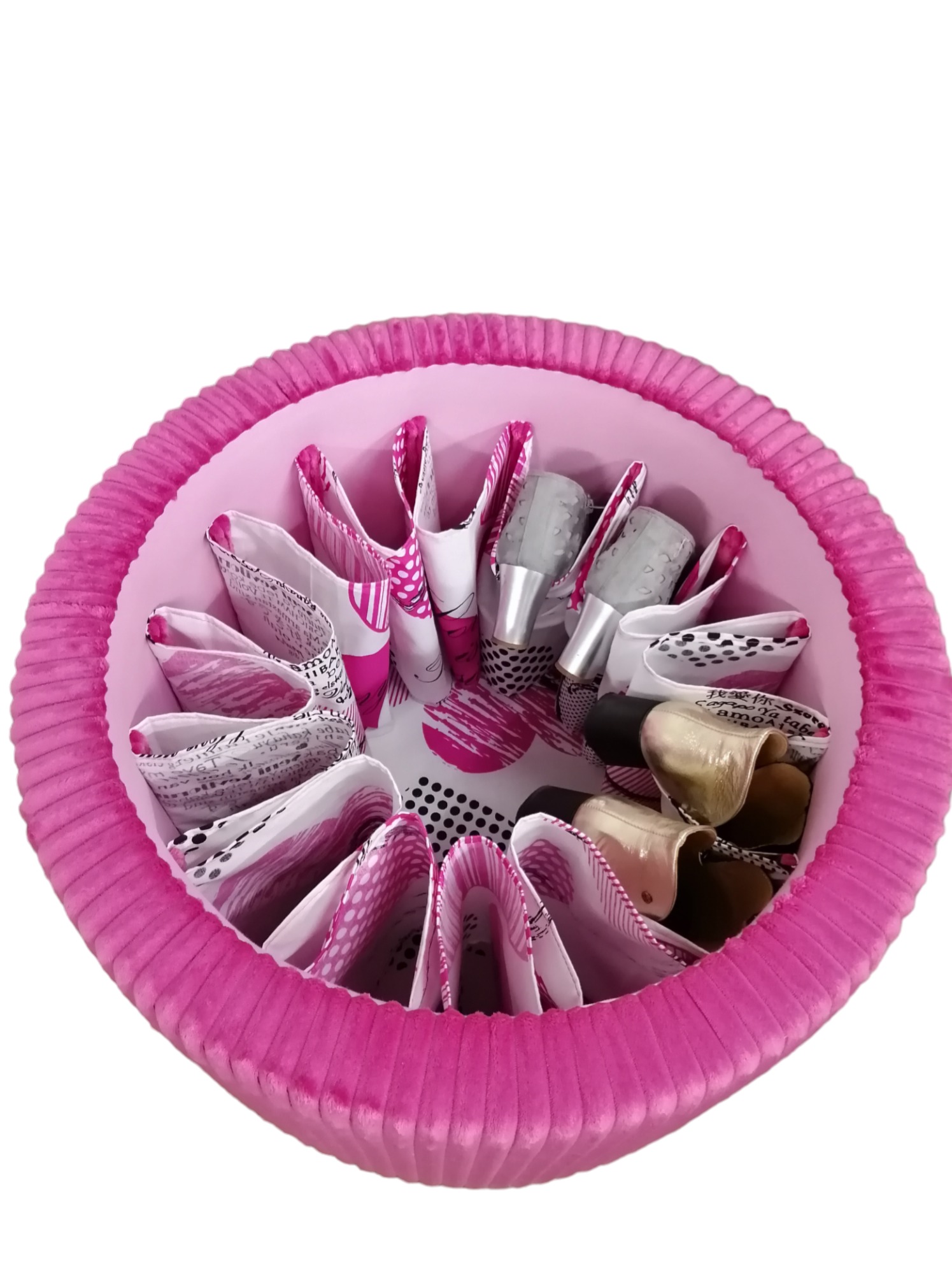 Ręcznie robiony, okrągły, tapicerowany puf w odcieniach różu, z przegródkami na buty wewnątrz, widoczne różne style i kolory obuwia.