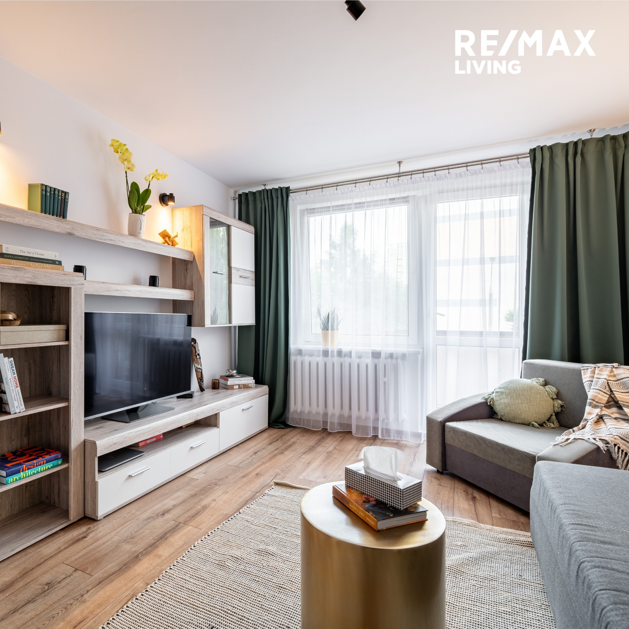 Jasne wnętrze salonu z drewnianą podłogą i meblami w odcieniach beżu i bieli, z akcentami zieleni w postaci zasłon i poduszki, złoty stolik kawowy z książką i pudełkiem chusteczek, dywan w stylu...