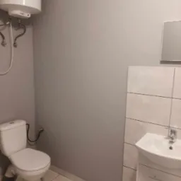 Nowoczesna łazienka z szarą ścianą, białymi płytkami, toaletą, umywalką z szafką i bojlerem.