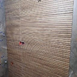 Ryszard Łaszewski - Ściana wyłożona płytkami imitującymi drewniane panele, z widocznymi gniazdkami elektrycznymi i rurami wodnymi, w trakcie prac wykończeniowych.