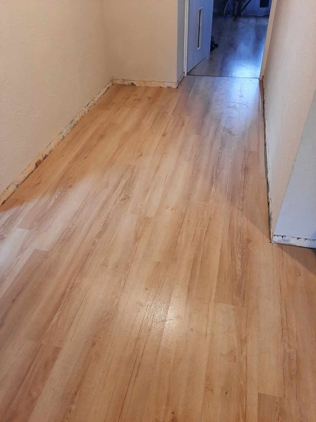 Nowo położone panele podłogowe w korytarzu, widoczne ślady po remoncie przy ścianach i otwarte drzwi w tle.
