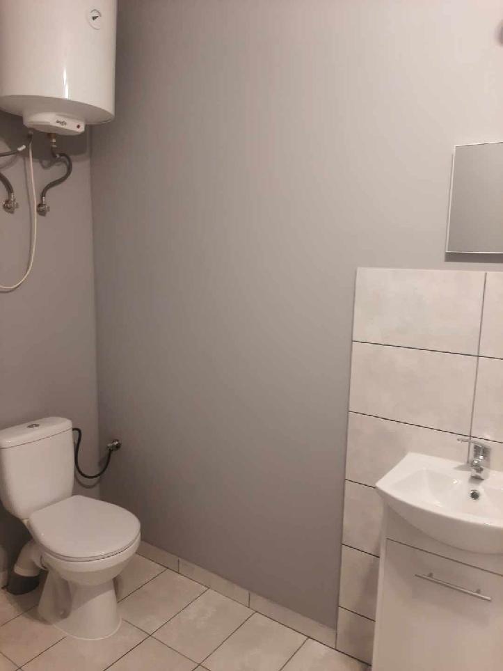 Nowoczesna łazienka z szarą ścianą, białymi płytkami, toaletą, umywalką z szafką i bojlerem.