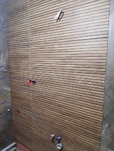 Ściana wyłożona płytkami imitującymi drewniane panele, z widocznymi gniazdkami elektrycznymi i rurami wodnymi, w trakcie prac wykończeniowych.