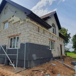 Gerbud - Ocieplenie grafitowym styropianem fragmentu elewacji domu jednorodzinnego z białego bloczka. Widoczne rusztowania, narzędzia i materiały budowlane.