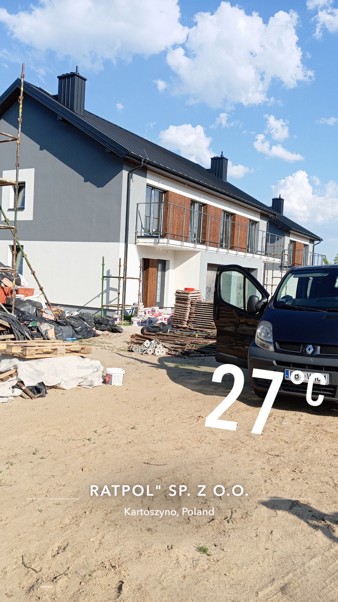 Dwukondygnacyjny dom w trakcie prac elewacyjnych. Widoczne rusztowania, materiały budowlane i samochód dostawczy. Część elewacji pomalowana na szaro i biało.