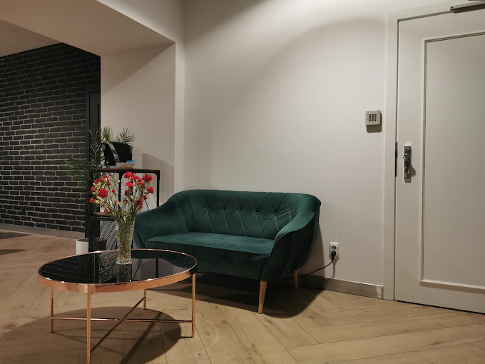 Nowoczesne wnętrze biurowe z zieloną sofą, stolikiem kawowym z kwiatami i ścianą z czarnej cegły.