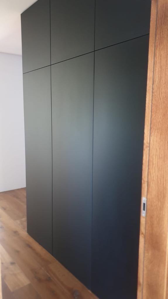 Czarna, minimalistyczna zabudowa szafy z ukrytymi uchwytami we Wrocławiu, dopasowana do drewnianej podłogi i framugi drzwi, z widocznymi subtelnymi liniami podziału frontów.