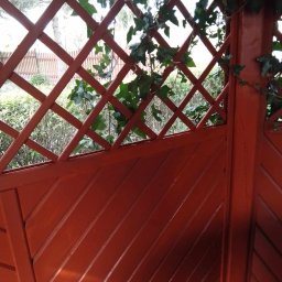 Lwica - Świeżo pomalowana, brązowa drewniana altana z kratką, porośnięta bluszczem, widok z bliska.