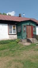 Dom jednorodzinny przed i po remoncie: biała, otynkowana ściana z oknem sąsiaduje z zieloną, drewnianą dobudówką z wejściem. Widoczne schody wejściowe i trawnik.