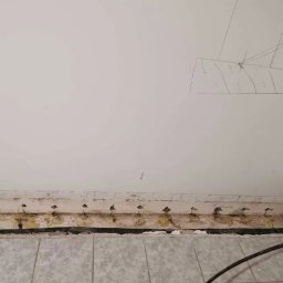 Przedsiębiorstwo Usługowo Handlowe JACEK CHMIELEWSKI - Przygotowany fragment ściany przy podłodze, z widocznymi otworami i elementami uszczelniającymi, prawdopodobnie przed nałożeniem warstwy izolacyjnej. Na ścianie widoczne prowizoryczne oznaczenia...