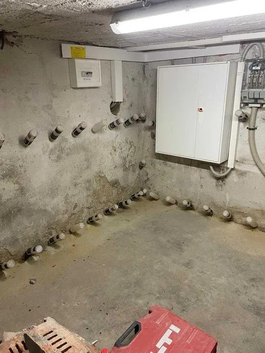 Piwnica z widocznymi nawierconymi otworami w ścianie, wypełnionymi preparatem iniekcyjnym, skrzynka narzędziowa Hilti w rogu.