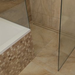 KOMREM SPÓŁKA Z OGRANICZONĄ ODPOWIEDZIALNOŚCIĄ - Nowoczesna łazienka z beżowymi płytkami, kabiną prysznicową typu walk-in z odpływem liniowym, wanną obudowaną mozaiką i podwieszaną toaletą.