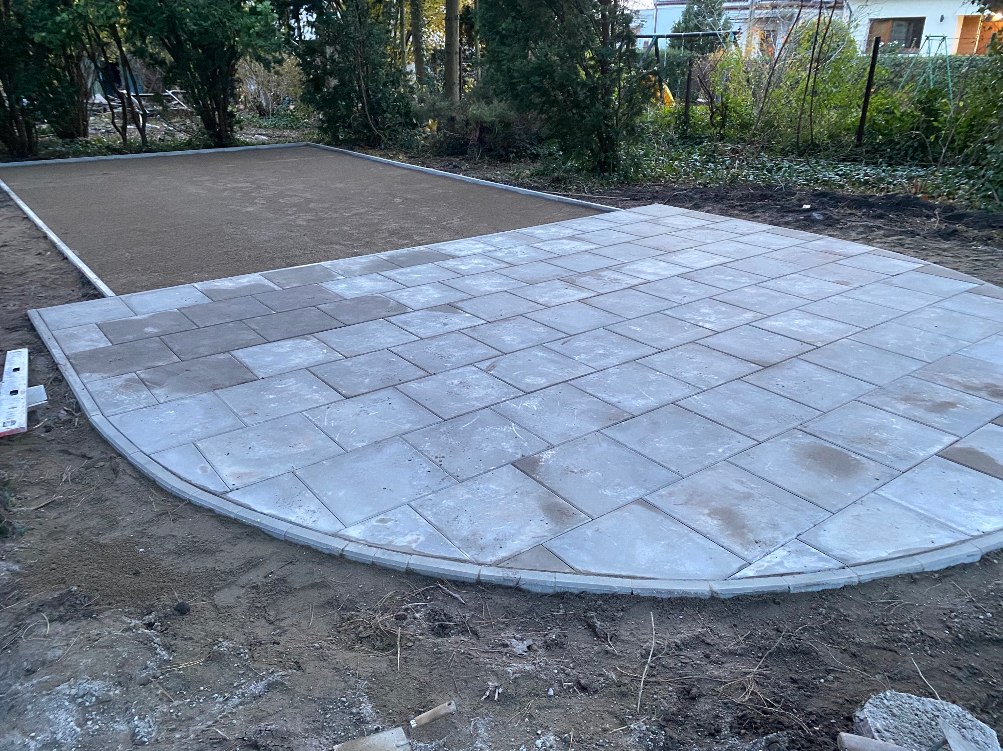 Układanie szarej kostki brukowej w kształcie półkola, obrzeża z kostki brzegowej, przygotowany teren pod dalszą część nawierzchni.